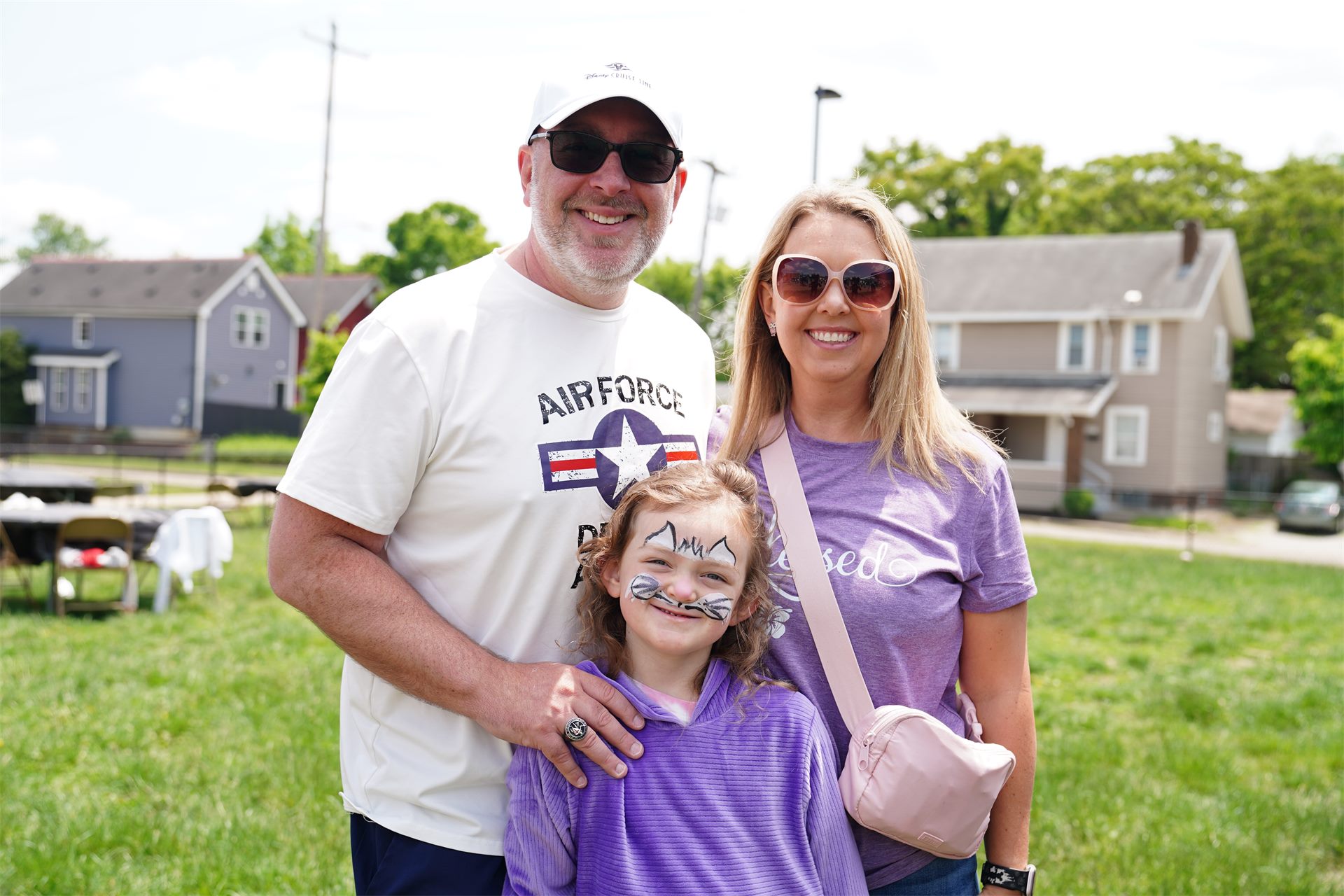A smiling family with their daughter, her face painted, at a neighborhood Sidewalk Sunday School event