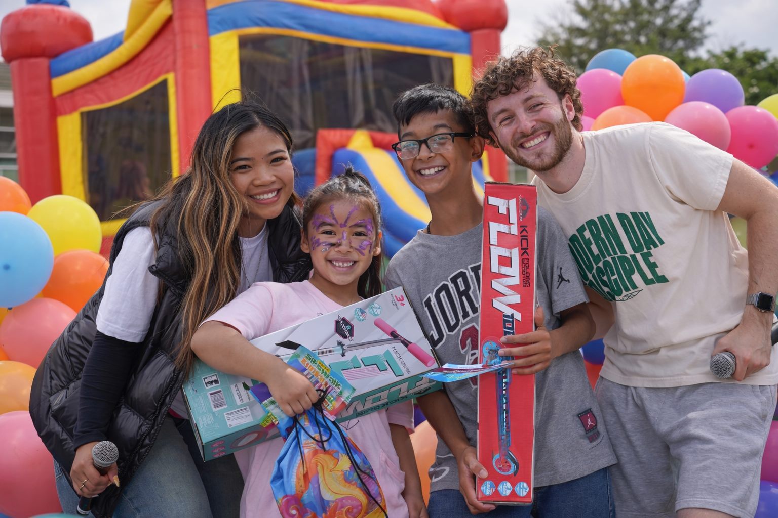 Smiling kids holding the scooters they won, with volunteers beside a bounce house